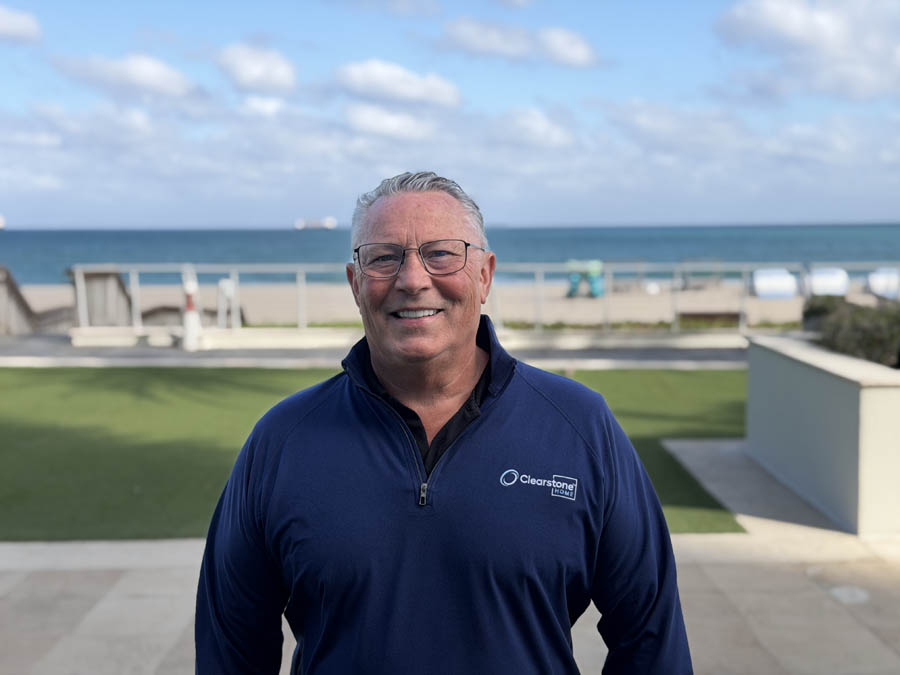 Man in blue jacket smiling near oceanfront background.